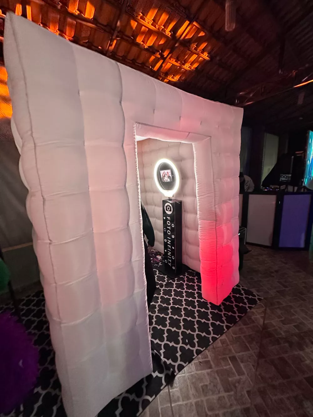 Cabine de fotos inflável branca da Foto Infinity com totem e ring light dentro, iluminada em festa